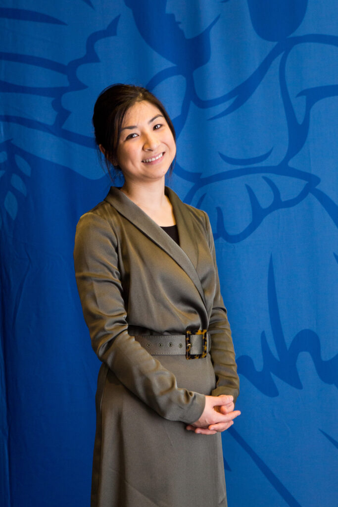 A photo of Dr Alexis Ceecee Britten-Jones smiling, standing in front of a blue background.